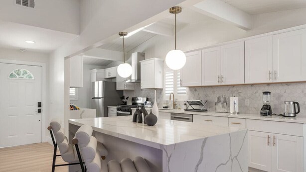 Cocina moderna con armarios blancos, una isla de mármol y una zona de asientos tipo bar.