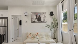 Un salon moderne avec un canapé, une petite table sur laquelle se trouvent un vase et une télécommande, et un tableau représentant une bataille spatiale.
