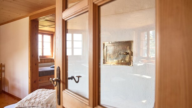 A wooden-framed door with a brass lock, a bed with a white blanket, and a window with a view of a wooden structure.