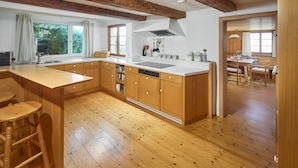 A kitchen with wooden cabinets, a large island with stools, a dishwasher, and a window with curtains.