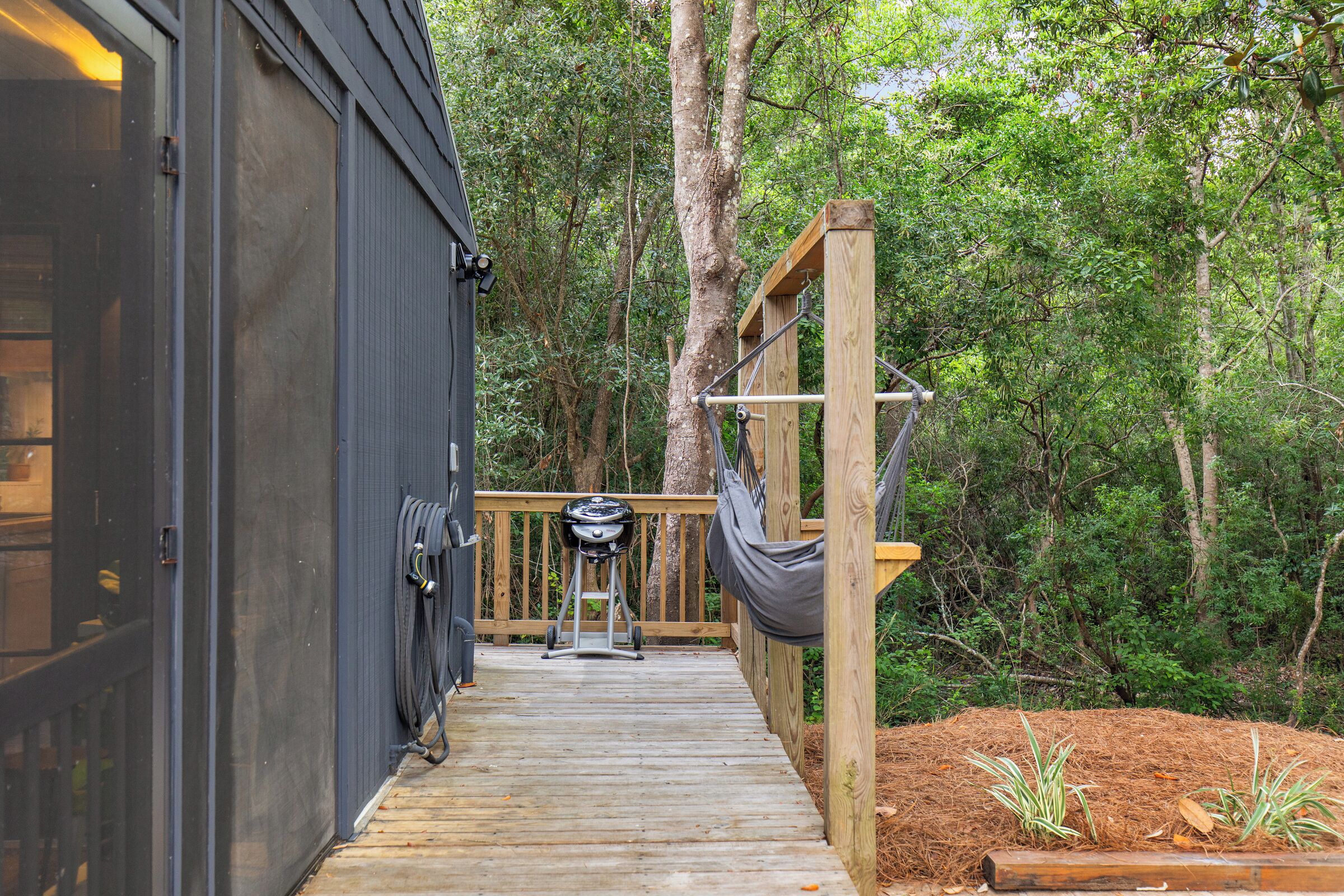 Une terrasse en bois menant à un bâtiment équipé d’un barbecue et d’un hamac.
