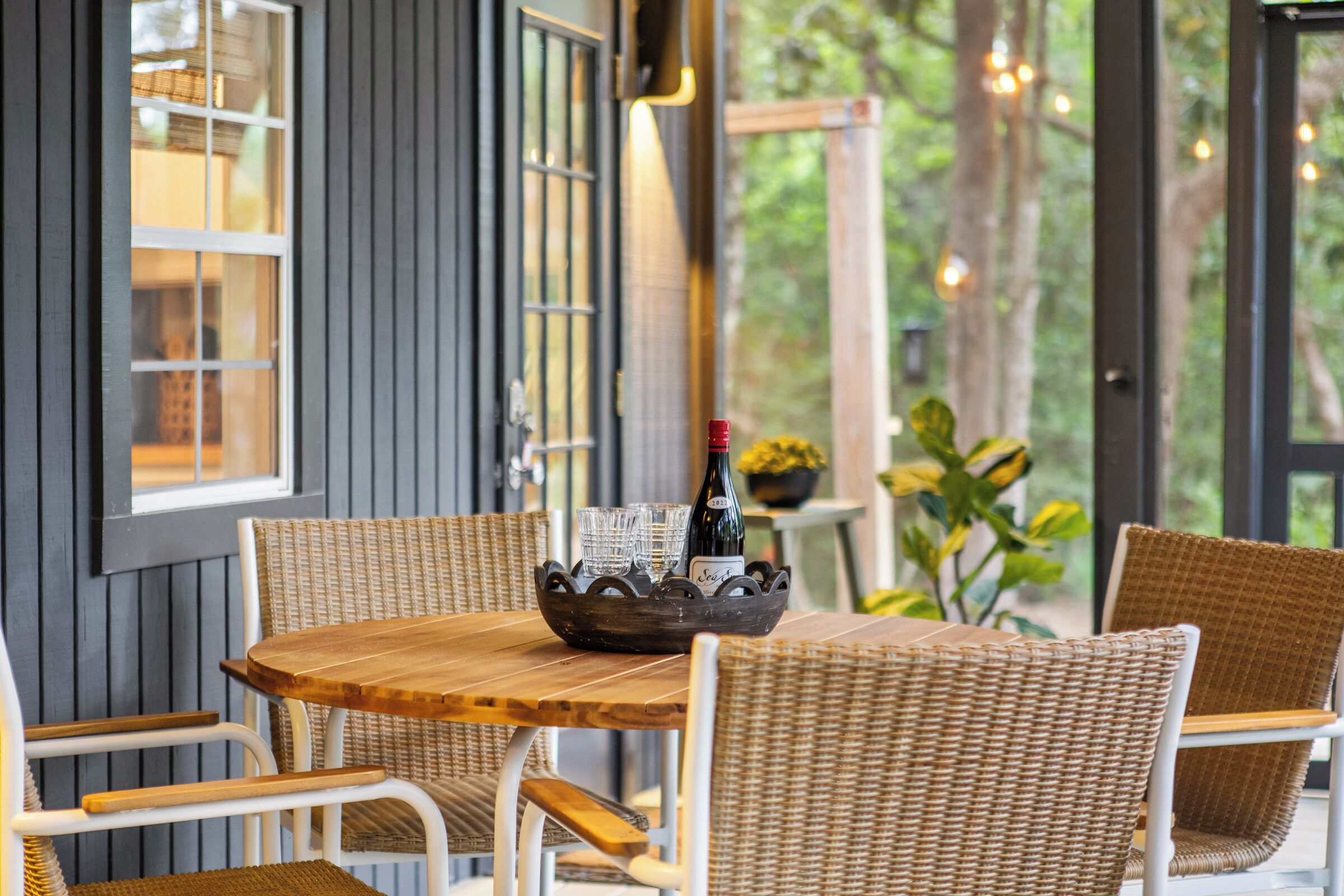 A wooden table with wicker chairs, a bottle of wine, and glasses on a tray.