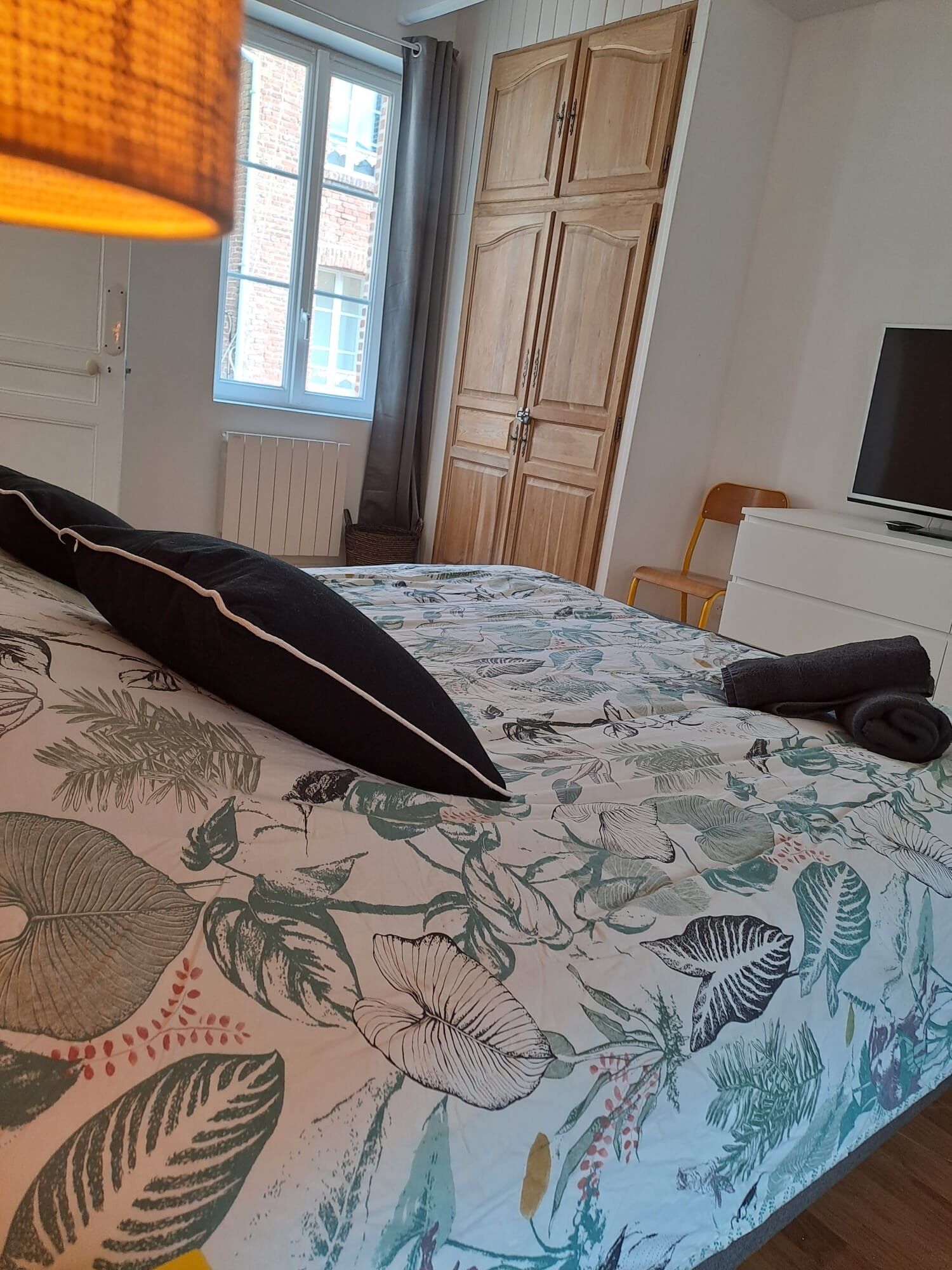 Une chambre à coucher avec un lit, une télévision, une armoire et une fenêtre avec des rideaux.