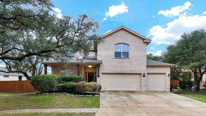 A two-story house with a brick facade, a garage, and a well-maintained lawn. - Spacious 5BR Retreat with Heated Pool & Outdoor Games (San Antonio)