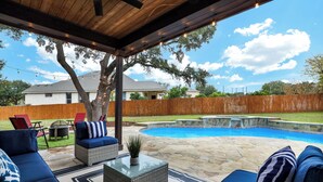 A backyard with a swimming pool, outdoor furniture, and a wooden deck. - Spacious 5BR Retreat with Heated Pool & Outdoor Games (San Antonio)
