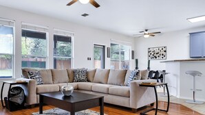 A modern living room with a sectional sofa, a coffee table, and a dining area with a bar stool. - Spacious 5BR Retreat with Heated Pool & Outdoor Games (San Antonio)