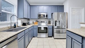 A modern kitchen with grey cabinets, stainless steel appliances, a granite countertop, and a window with blinds. - Spacious 5BR Retreat with Heated Pool & Outdoor Games (San Antonio)