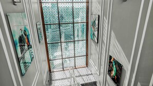 A modern hallway with a glass door leading to a balcony, framed artwork on the walls, and a light fixture.