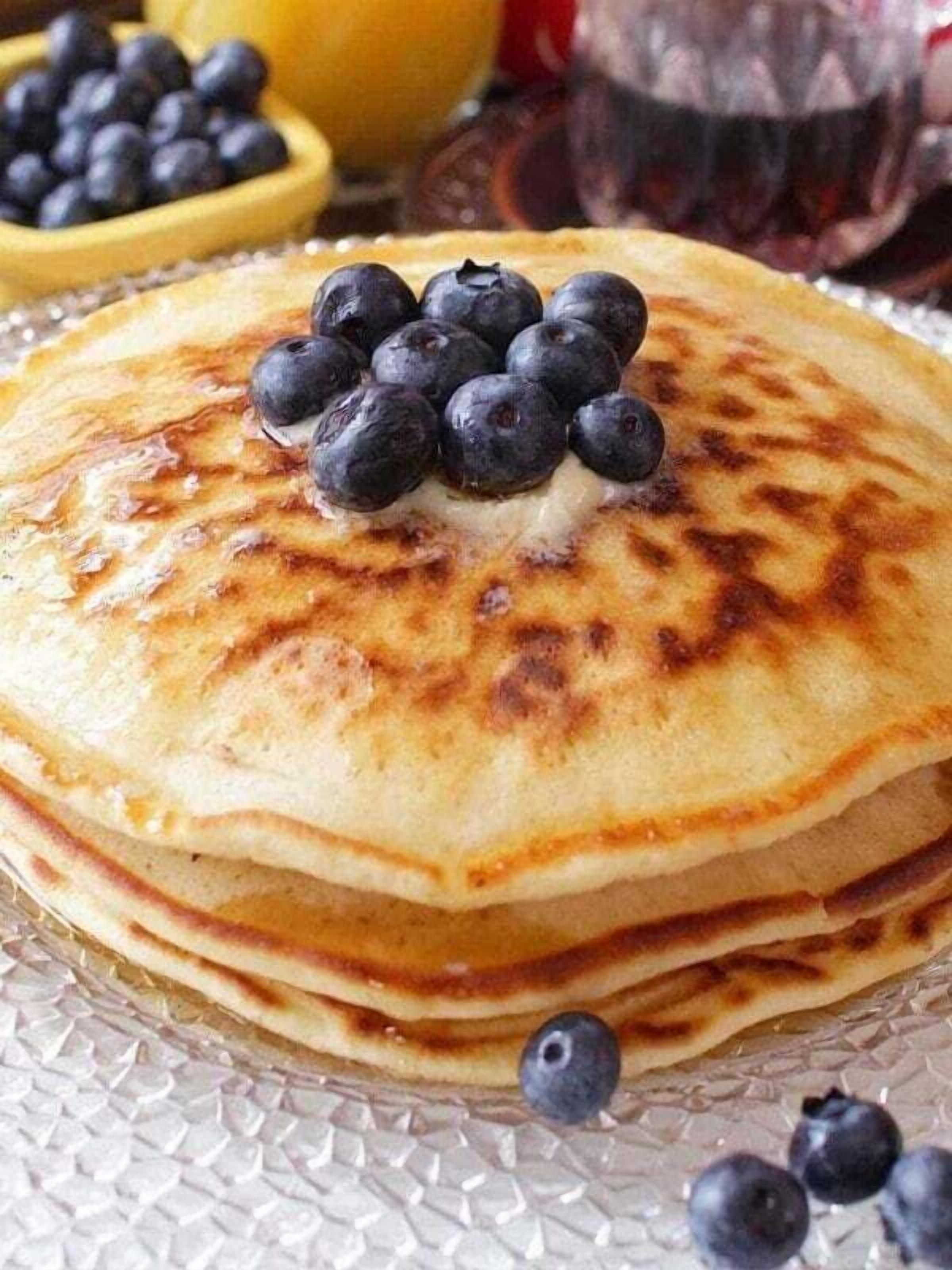 A stack of pancakes topped with blueberries and a small bowl of blueberries in the background.