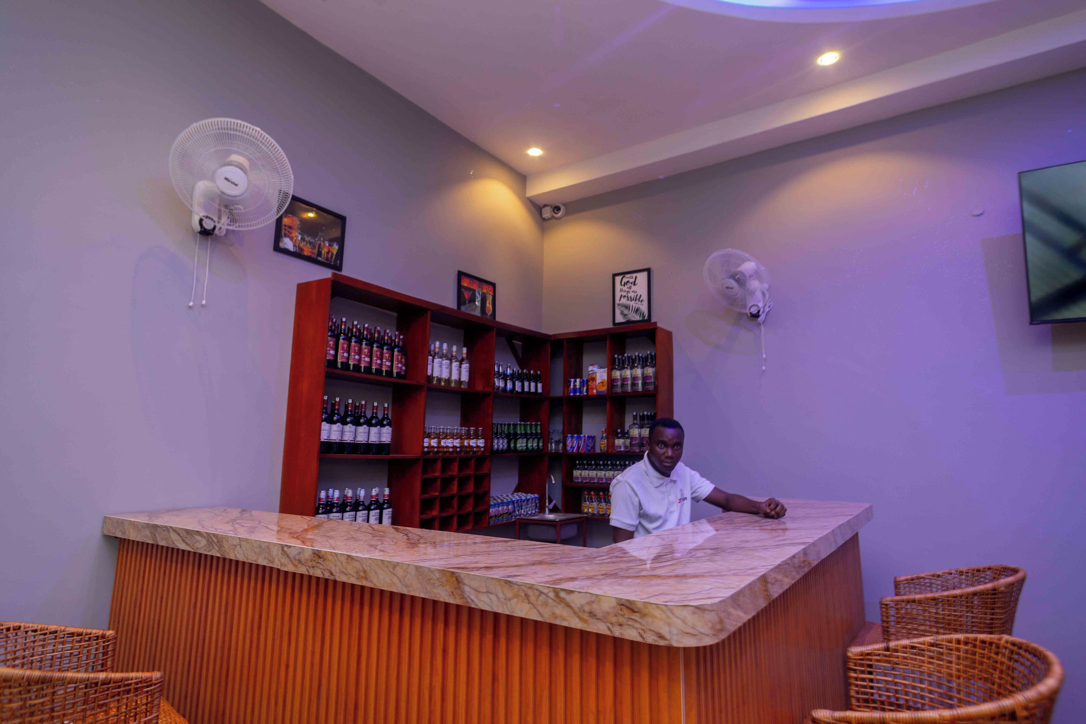 Un espace bar doté d'un comptoir en marbre, de chaises en osier et d'étagères remplies de bouteilles.