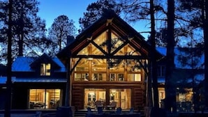 A log cabin with a large front porch and multiple windows, surrounded by trees.