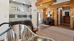 A modern bathroom with a glass shower enclosure, wooden beams, and a rustic kitchen area with wooden cabinets and a stone countertop.