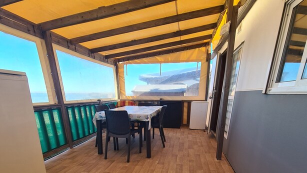 A covered outdoor dining area with wooden flooring, tables, and chairs.