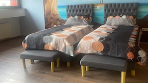A bedroom with a bed featuring a tufted headboard, a large mural of a beach scene, and a hanging light fixture. - Beautiful, large penthouse for a maximum of 4 people. Kitchen including all utensils (Wadgassen)