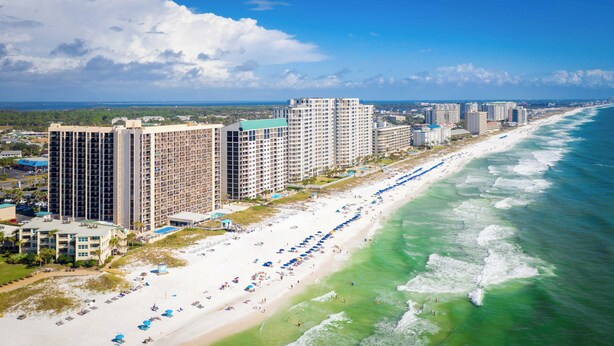 Ein Küstenhotel mit mehreren Hochhäusern, einem Strand mit Sonnenschirmen und Blick auf den Ozean.