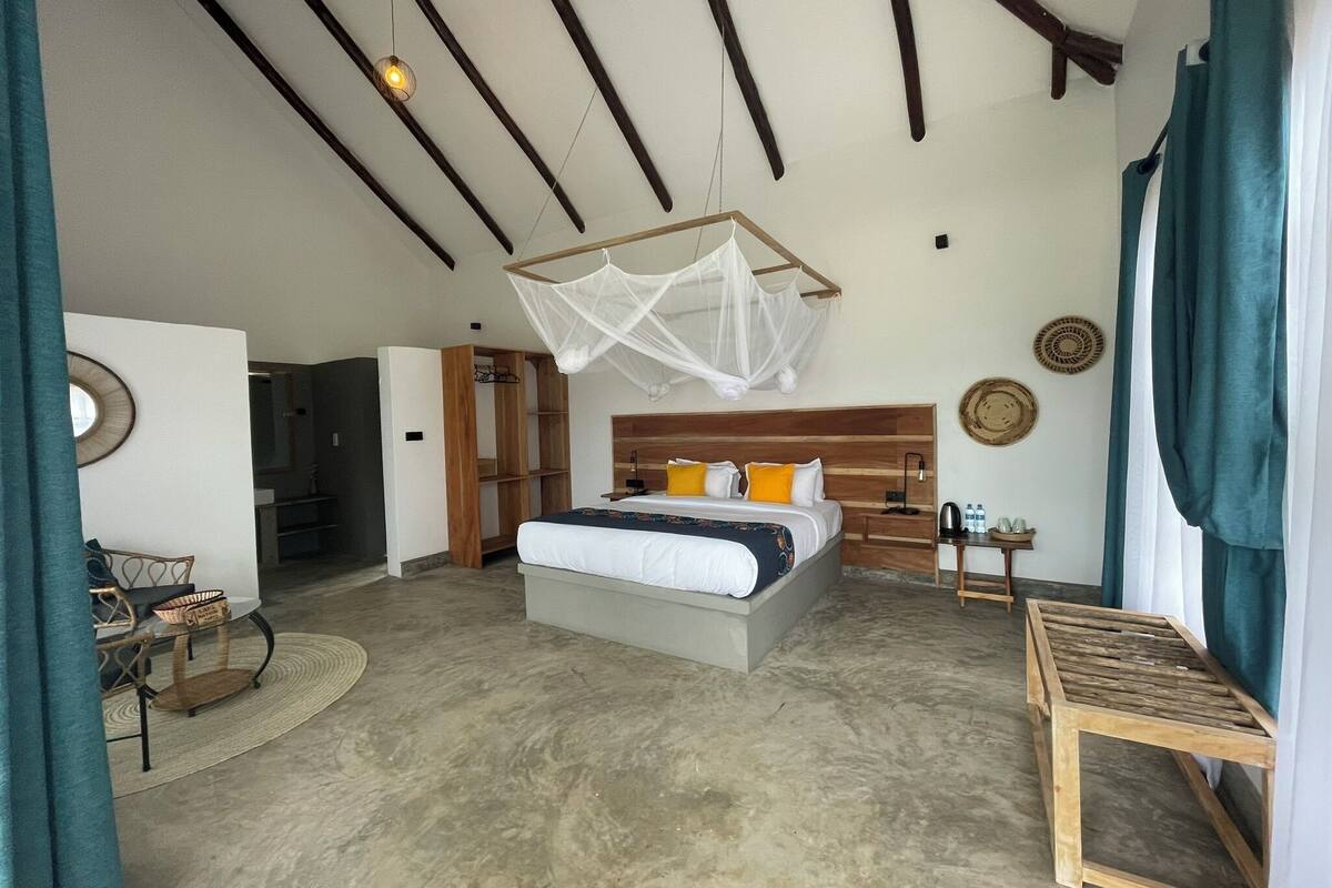 A spacious bedroom with a large bed, wooden headboard, bedside tables, and a hanging mosquito net.