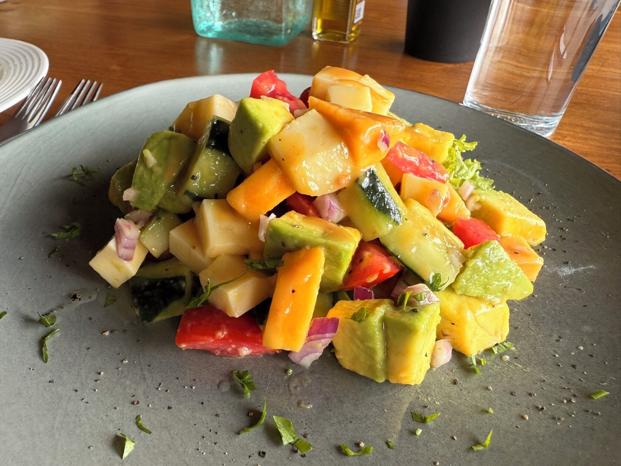 A plate of diced fruit salad with visible pieces of mango, avocado, and red bell pepper.