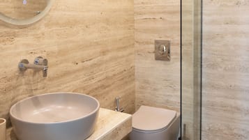 A modern bathroom with a round sink, toilet, and glass shower enclosure.
