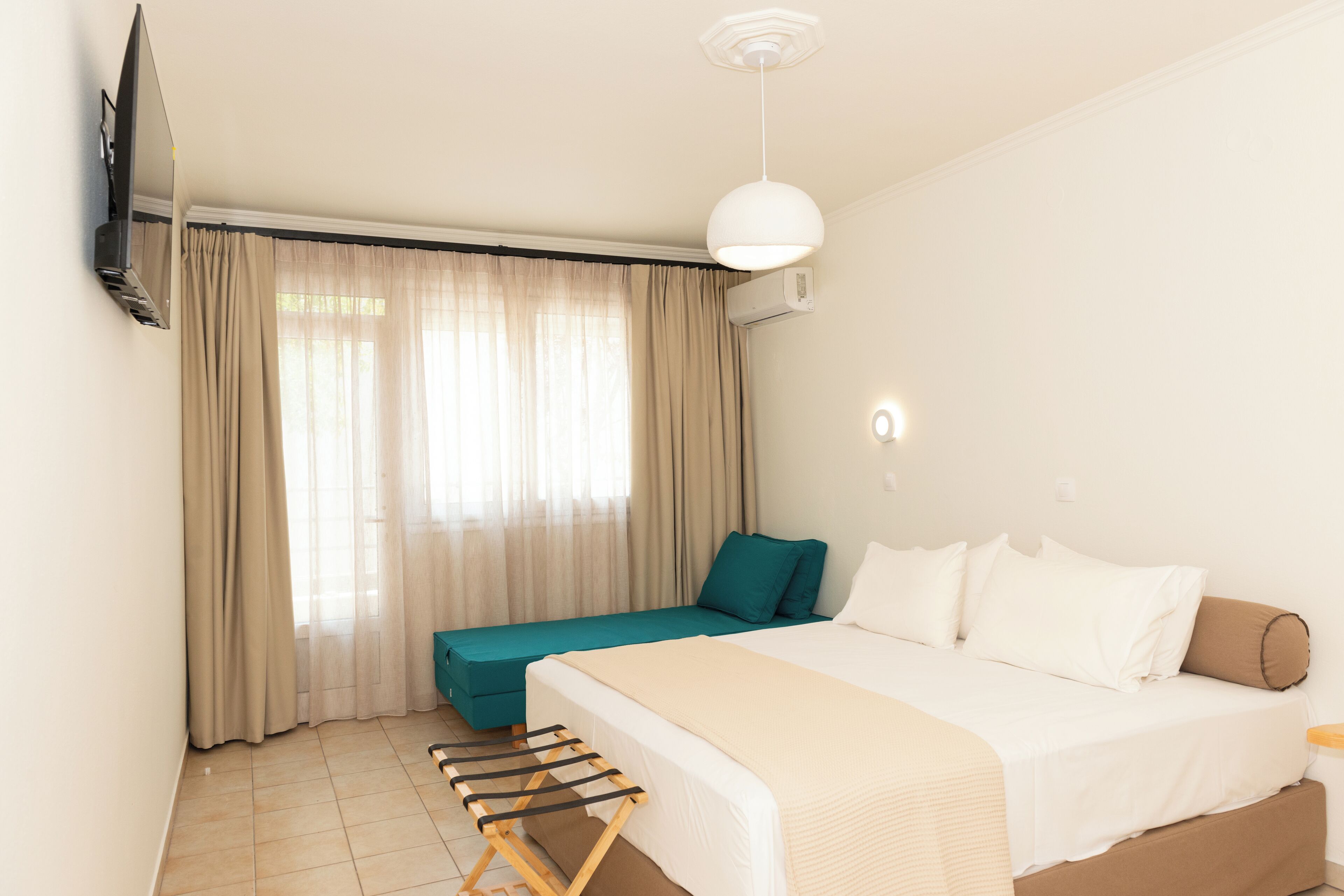Una habitación de hotel con cama, zona de estar, televisor montado en la pared y luz de techo.