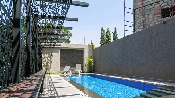 A swimming pool with a geometric tile pattern, surrounded by a concrete deck and a metal fence with intricate cutouts.
