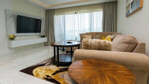 A modern living room with a flat-screen TV, a sofa, a coffee table, and a patterned rug.