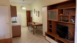 Uma cozinha compacta com fogão a gás, mesa de jantar com cadeiras e televisão sobre um suporte de madeira.