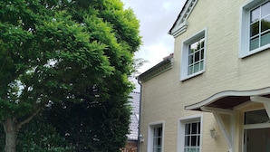 A patio area with wooden chairs and a table, surrounded by greenery and a house with a white facade and windows. - Villa Scharbeutz Pönitz, spacious, quiet, central (Scharbeutz)