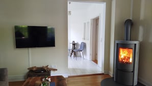 A living room with a flat-screen TV, a wooden coffee table with decorative items, a stone fireplace, and a view into the dining area. - Villa Scharbeutz Pönitz, spacious, quiet, central (Scharbeutz)