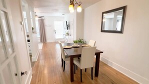 Un comedor con suelo de madera, una mesa de madera oscura y sillas blancas.