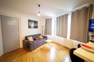 Una sala de estar moderna con un sofá gris, una mesita blanca y un televisor sobre un mueble.