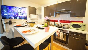 Una cocina moderna con un televisor de pantalla plana, una zona de comedor con sillas y un microondas.