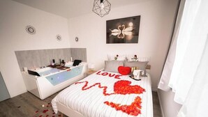 Un dormitorio moderno con una cama grande, una bañera independiente y una obra de arte colgada en la pared.