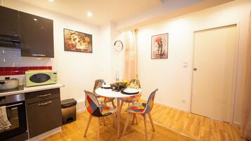 Cocina compacta con microondas, estufa y armarios. Hay una mesa de comedor con sillas y un reloj en la pared.