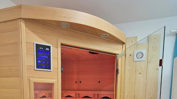 Una sauna con panel de control, bancos de madera y puertas de vidrio.