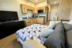 A compact living space with a kitchenette, a bed with patterned bedding, and a television.