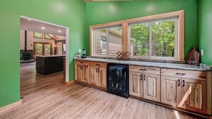 A kitchen with wooden cabinets, a built-in dishwasher, and a large window with a view of trees. - NEW 4-bedroom home, private, hot tub, fenced yard, pet friendly (Hawley)