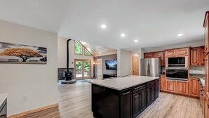 A spacious kitchen with a large island, wooden cabinets, and a stone fireplace. - NEW 4-bedroom home, private, hot tub, fenced yard, pet friendly (Hawley)