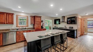 A modern kitchen with wooden cabinets, a large island, and a view of the outdoors. - NEW 4-bedroom home, private, hot tub, fenced yard, pet friendly (Hawley)