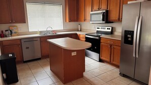 A kitchen with wooden cabinets, a stainless steel refrigerator, a microwave, and a dishwasher. - Charming 2-bedroom townhome in beautiful Riverview with WiFi, AC (Riverview)