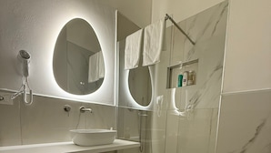 Un baño moderno con un lavamanos blanco, espejo y cabina de ducha con mampara de vidrio.