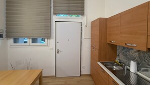 Una cocina pequeña con armarios de madera, una puerta blanca y un ventanal con persianas.