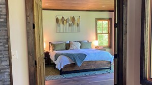 Une chambre à coucher avec un cadre en bois, un lit, une œuvre d’art accrochée au mur et une fenêtre.
