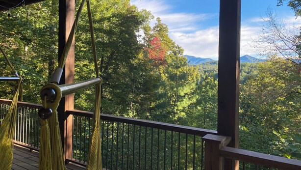 Une terrasse en bois avec un hamac et une rambarde en métal, offrant une vue sur un paysage montagneux boisé.