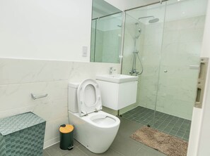Ein modernes Badezimmer mit Toilette, Waschbecken und einer Dusche in Glaswand.