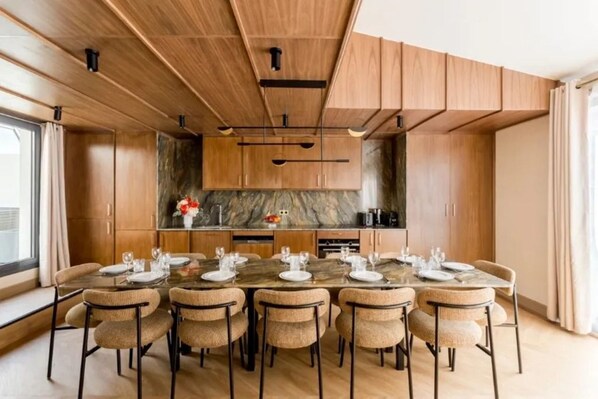 Una cocina moderna con armarios de madera, salpicadero de mármol y comedor con mesa de vidrio y sillas de mimbre.