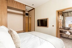 Un dormitorio con cama, armario, televisión y un baño visible a través de una puerta abierta.