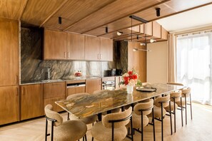 A modern kitchen with wooden cabinets, a marble countertop, and a dining area with wicker chairs.