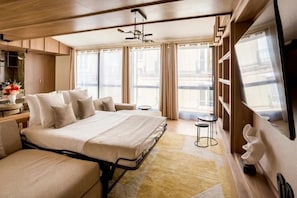 A modern hotel room with a large bed, a sofa, a small table, and a TV.