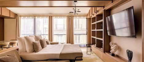 Habitación de hotel moderna con una cama grande, un sofá, un televisor y vistas a la ciudad.
