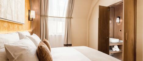 Habitación de hotel con una cama grande, cabecera de madera, tocador con espejo y armario.